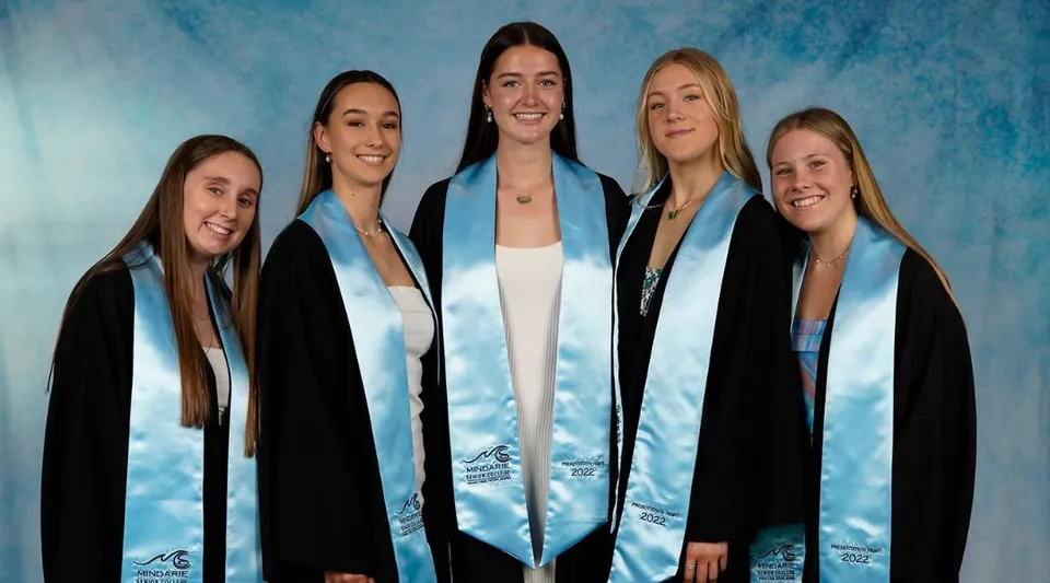 Cinque studentesse in toga da diploma nera sono in piedi davanti a uno sfondo blu al Mindarie Senior College.