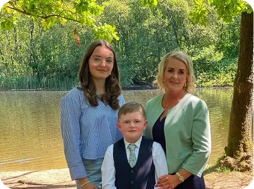Una ragazza, un bambino e una donna posano insieme accanto a uno stagno in un parco