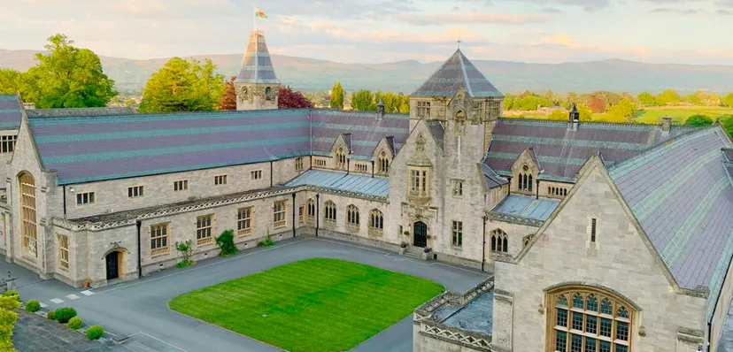 Il castello dall'aspetto medievale del Myddelton College con torri e un cortile interno verde sullo sfondo delle montagne.