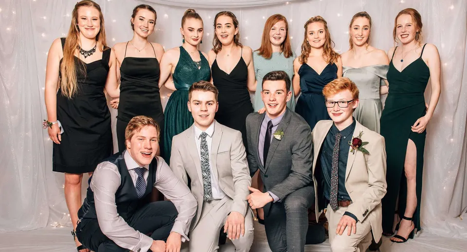 Un gruppo di studenti della Logan Park High School posa insieme su uno sfondo bianco, vestiti in abiti formali.