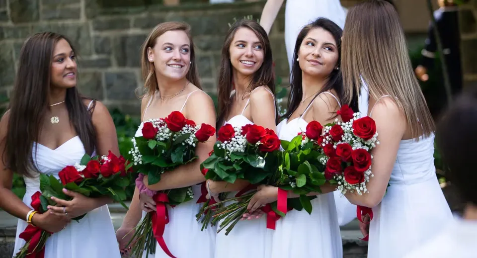 Un gruppo di studentesse della Holy Child Secondary School è davanti a un edificio in mattoni in abito bianco con grandi mazzi di rose rosse.
