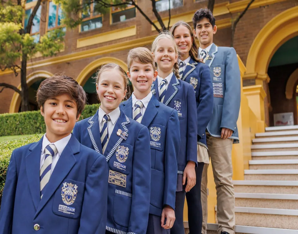 Sei studenti della Reddam House in divisa scolastica sorridono in fila su una scalinata davanti all'edificio.