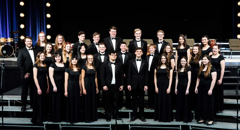 Un grande gruppo di studenti della Oakland Christian School in abito formale su un palco sotto i riflettori.