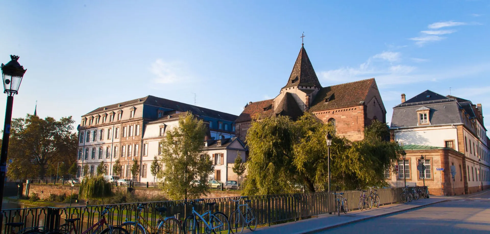 Sullo sfondo del Collège Episcopal Saint Étienne si vede una chiesa storica con un alto campanile, circondata da vecchi edifici e da una recinzione in ferro battuto.