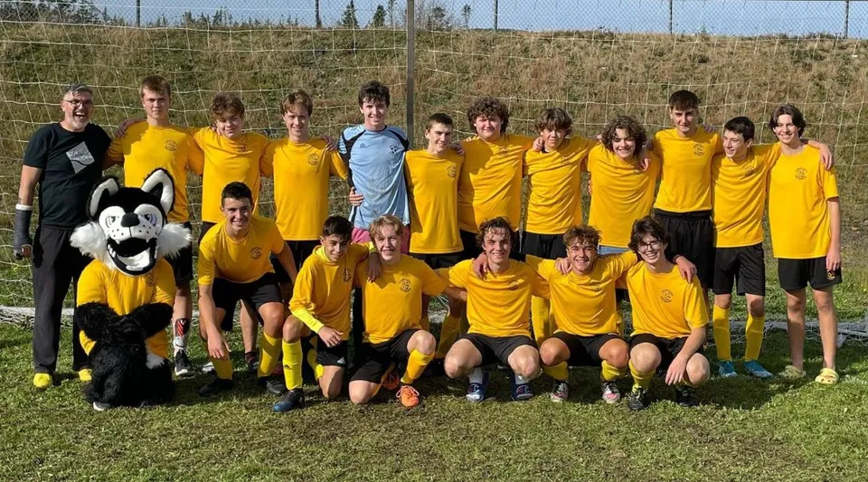Un gruppo di giovani calciatrici e calciatori in maglia gialla posa su un campo da gioco nel campus del Crescent Collegiate.