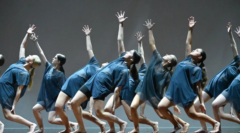 Studenti del Mahurangi College eseguono una performance di danza sincronizzata su un palco scuro, indossando costumi blu.