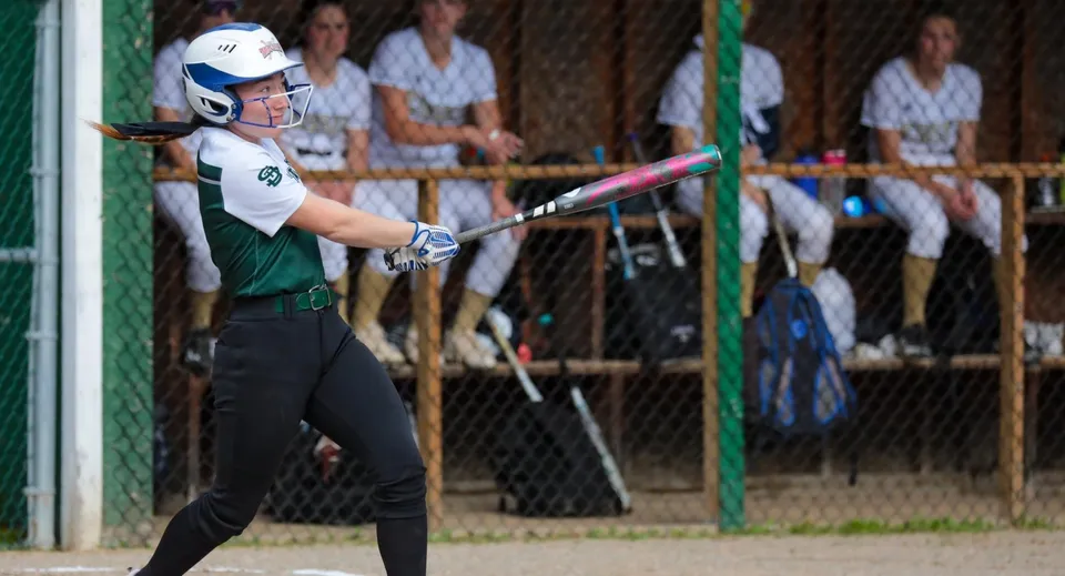 Una giocatrice di softball della St. Johnsbury Academy batea davanti alla panchina della squadra.