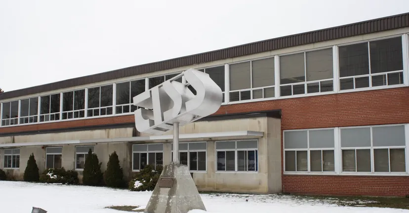 L'edificio moderno della Thousand Islands Secondary School con una scultura in primo piano e alberi innevati in inverno.