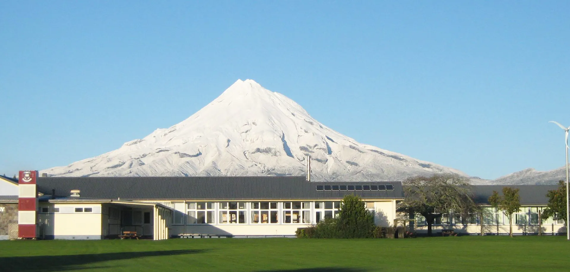 Un moderno edificio scolastico dell'Inglewood High School con grandi finestre davanti a una cima montuosa innevata.