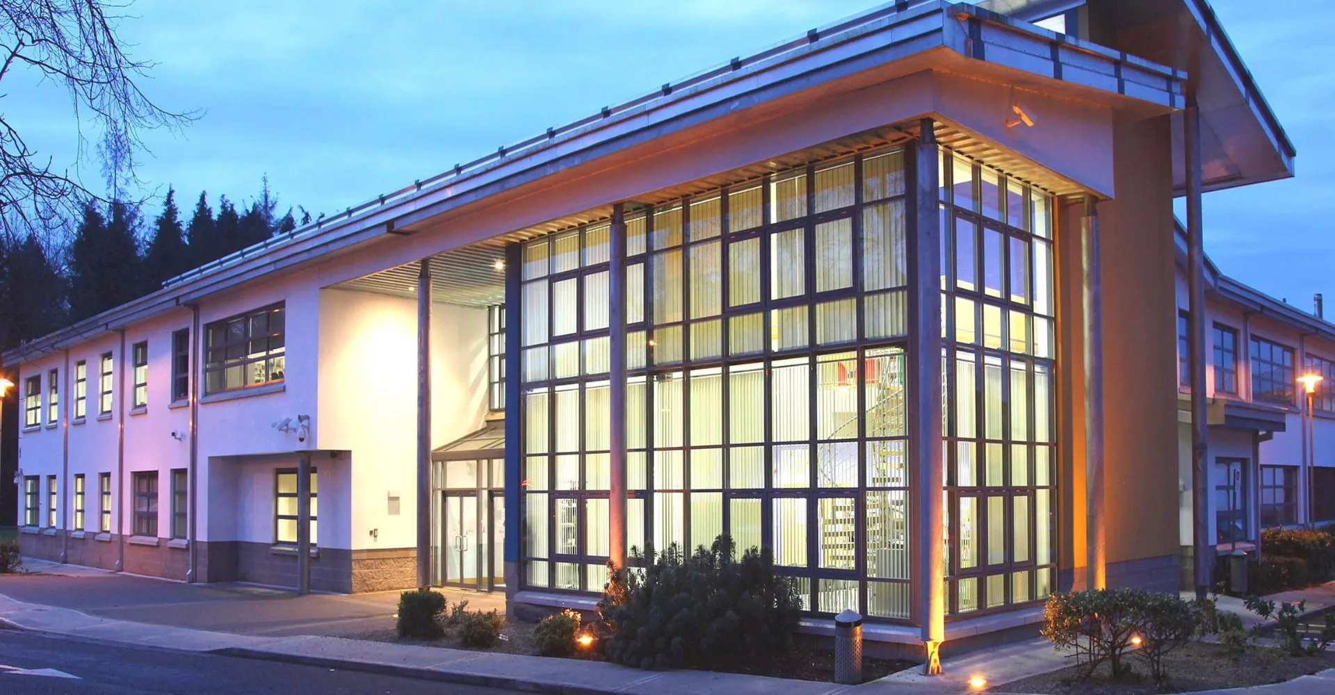 L'edificio dal design moderno con facciata in vetro e tetto spiovente del Largy College si trova in una zona boscosa ed è illuminato di sera.