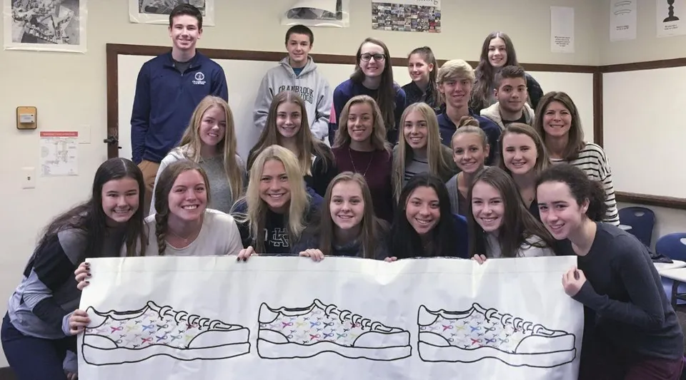 Un gruppo di studenti e studentesse della Cranbrook Schools tiene uno striscione con il disegno di un gatto all'interno di un ambiente chiuso.