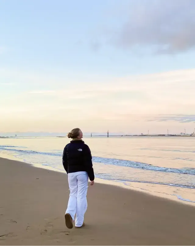Studentessa cammina sulla spiaggia in riva al mare al tramonto