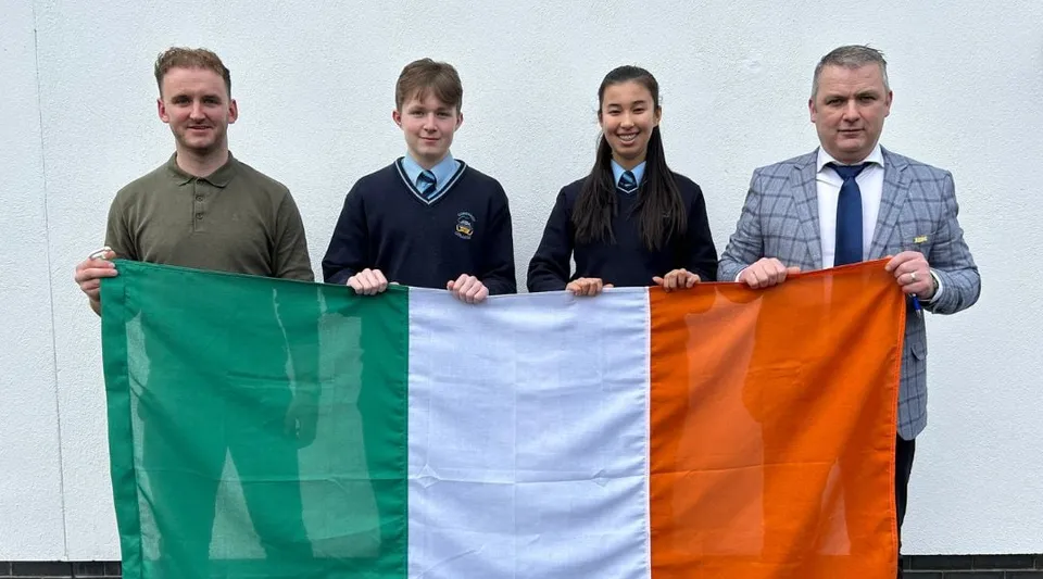 Quattro persone tengono la bandiera irlandese davanti a uno sfondo bianco nel campus del Comeragh College.