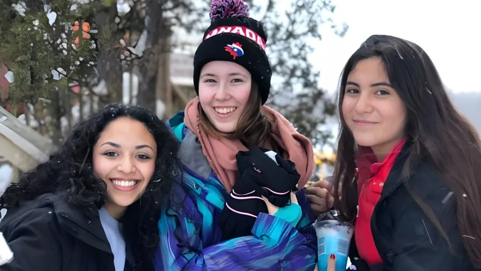 Tre studentesse della École Sainte-Anne posano insieme all'aperto davanti a un bosco innevato.