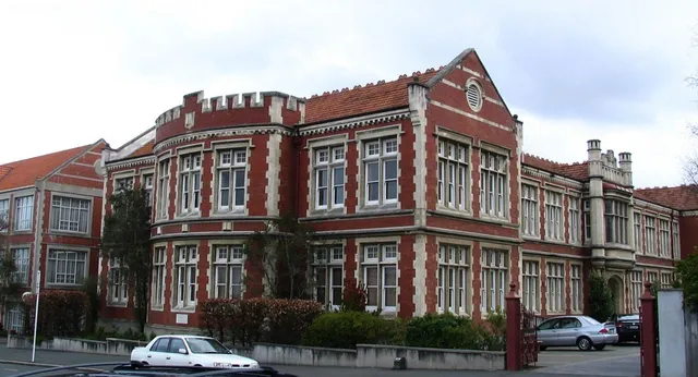L'edificio principale storico della Otago Girls High School è circondato da alberi e auto parcheggiate.