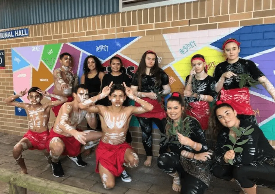 Un grupo de estudiantes de la Cardiff High School se encuentra frente a un mural colorido en una pared de ladrillo.