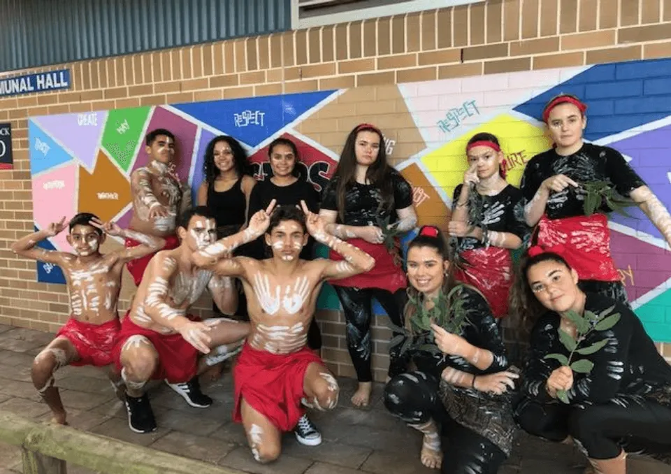 Un gruppo di studenti della Cardiff High School sta davanti a un murale colorato su una parete di mattoni.