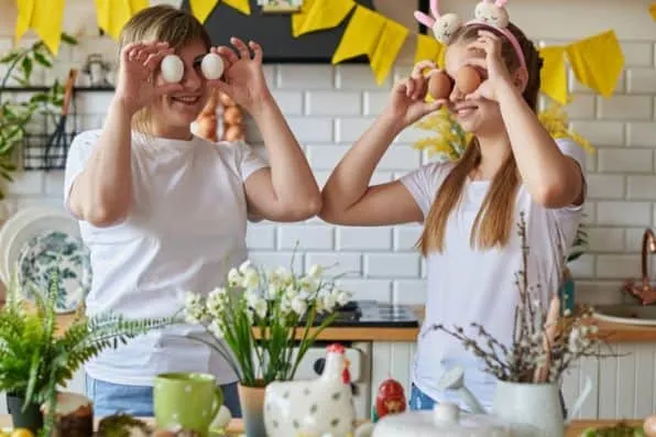Mujer y chica se tapan los ojos con huevos en una cocina decorada para Pascua