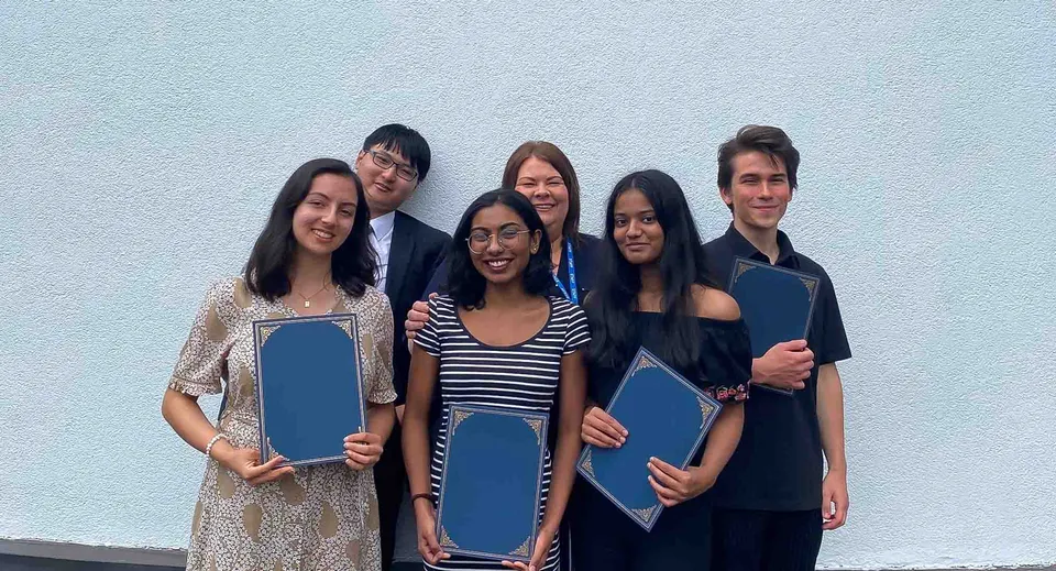 Un gruppo di studenti della Westbourne School è in piedi davanti a uno sfondo azzurro tenendo in mano delle cartelle blu.