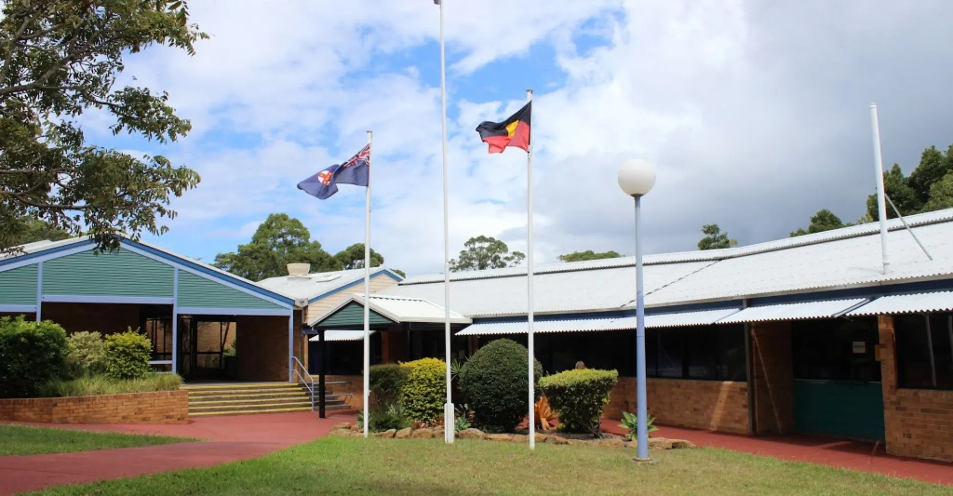 L'edificio della Kingscliff High School è circondato da una fitta vegetazione e mostra la bandiera australiana e un'altra bandiera.