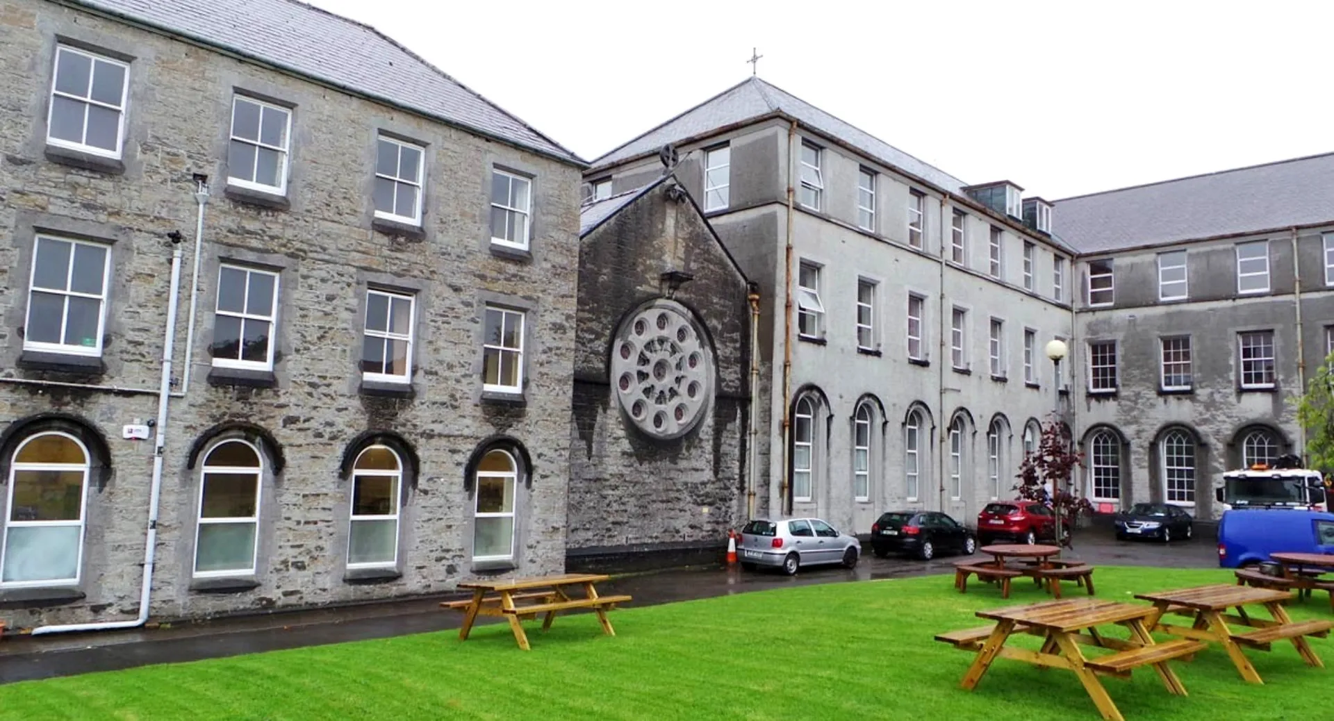 L'edificio dell'Ursuline College Sligo con finestra circolare e finestre ad arco circondato da un prato con tavoli da picnic.