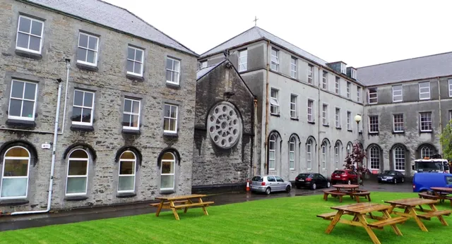 L'edificio dell'Ursuline College Sligo con finestra circolare e finestre ad arco circondato da un prato con tavoli da picnic.