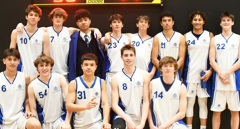 Un gruppo di giovani giocatori di basket in divisa posa davanti al tabellone segnapunti nel campus del Saint Kentigern College.