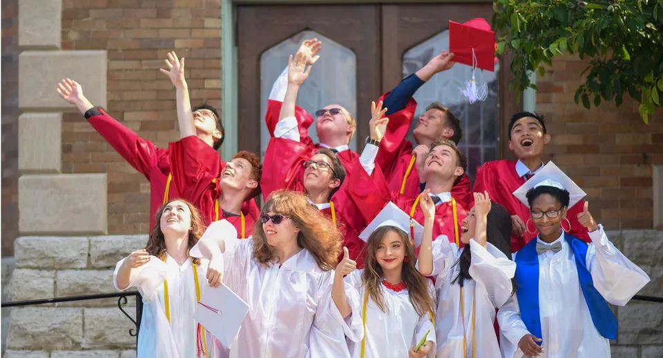 Un gruppo di diplomati della Dominion Academy of Dayton festeggia il proprio diploma davanti a un edificio in mattoni.