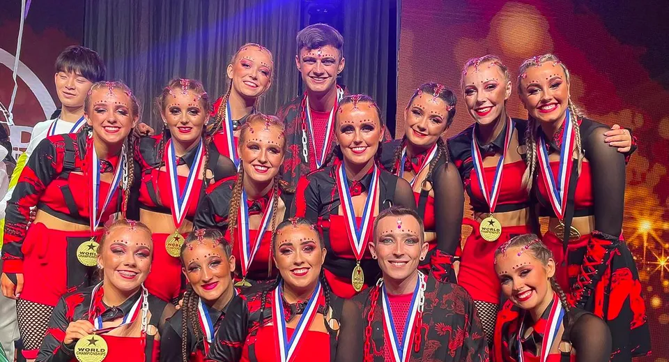 Un gruppo di studentesse e studenti della St. Louis Secondary School Dundalk posa sul palco in costumi rossi e neri.
