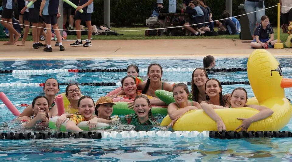 Un gruppo di studentesse della Kingaroy State High School si raccoglie in una piscina davanti a degli spettatori e a una rete da pallavolo.