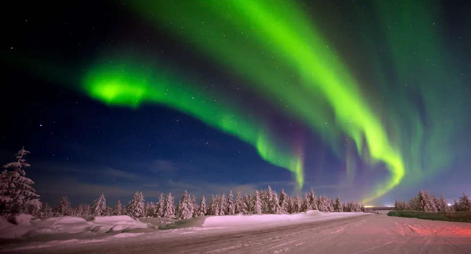 L'aurora boreale illumina il cielo notturno sopra un paesaggio boschivo innevato vicino alla Oromocto High School.