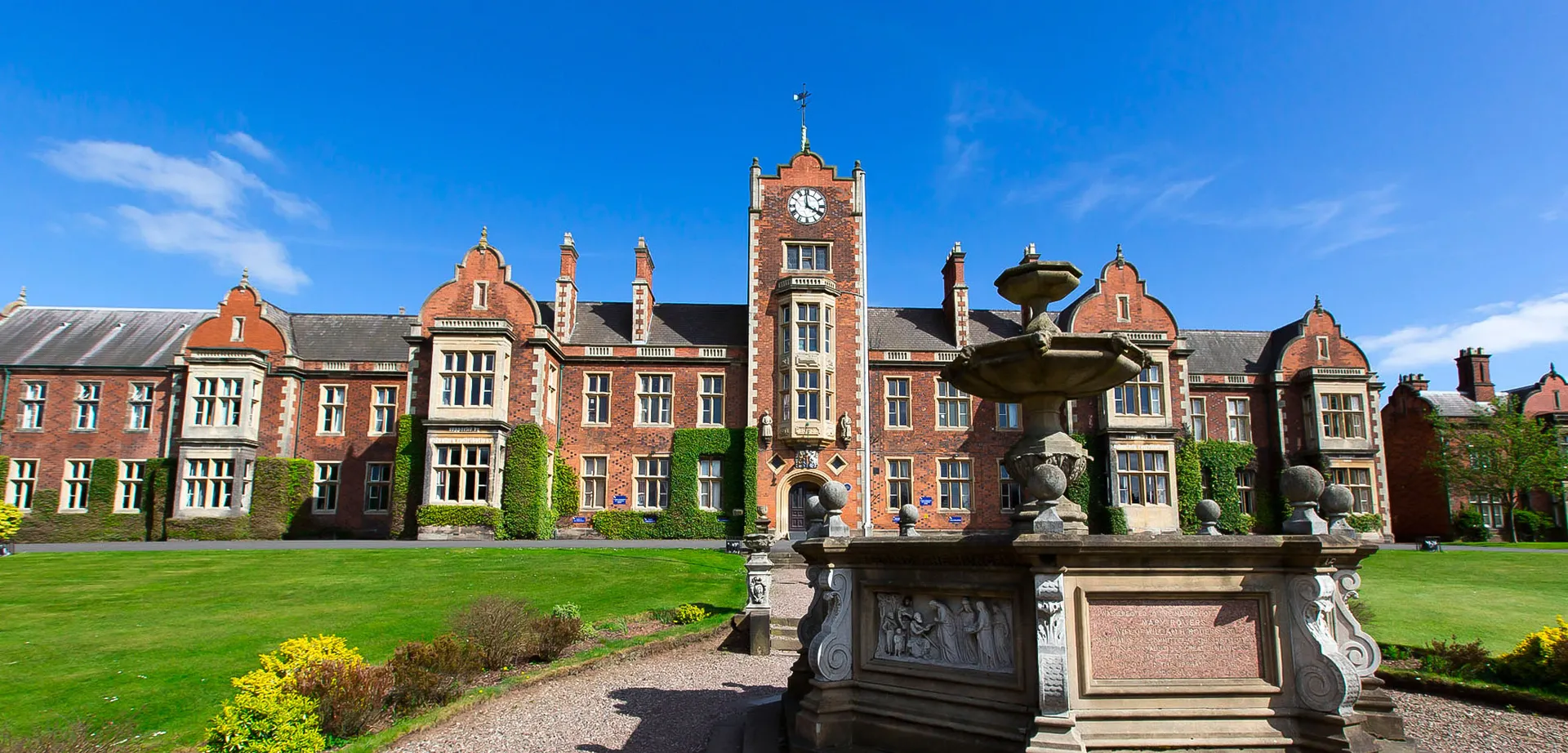 L'edificio storico con la torre dell'orologio della The Royal School Wolverhampton si trova in un giardino ben curato con una fontana.
