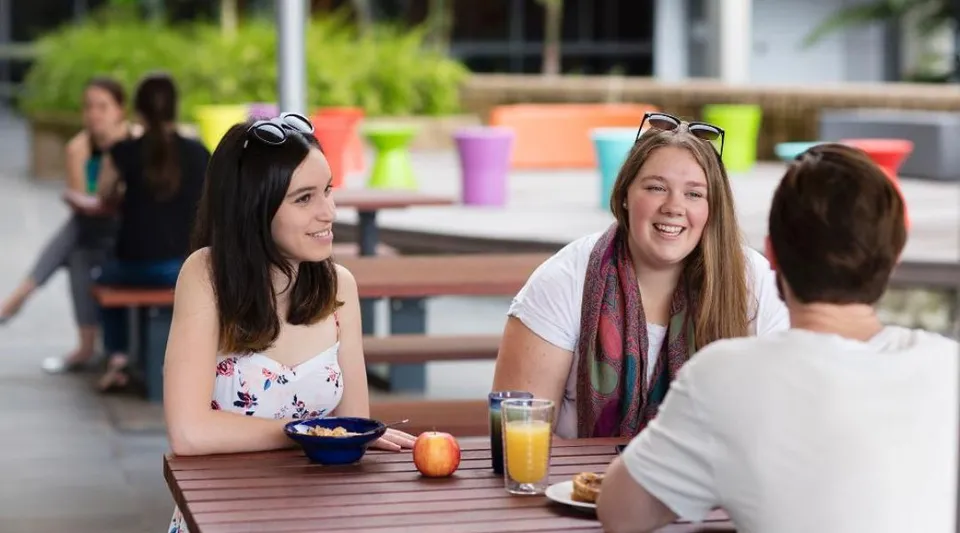Studenti della Wollongong University si godono un pasto all'aperto davanti a uno sfondo colorato.