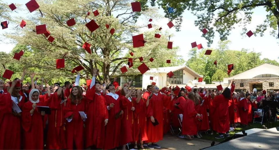 Diplomati della The Hun School of Princeton si radunano all'aperto in toghe rosse sotto alberi con decorazioni rosse.