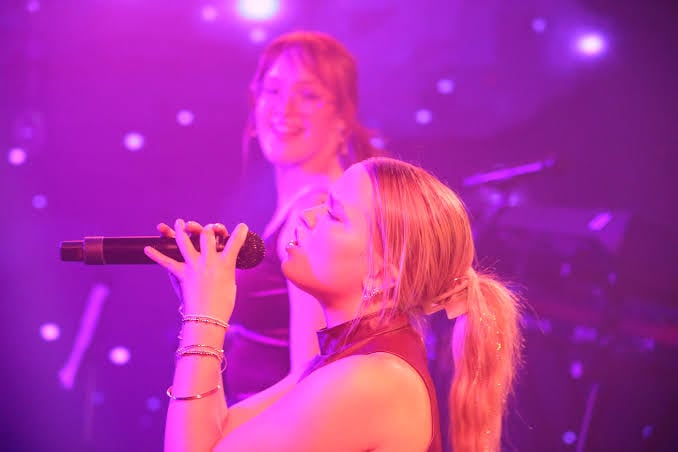 Eine Schülerin singt auf der Bühne mit pinkem Scheinwerferlicht