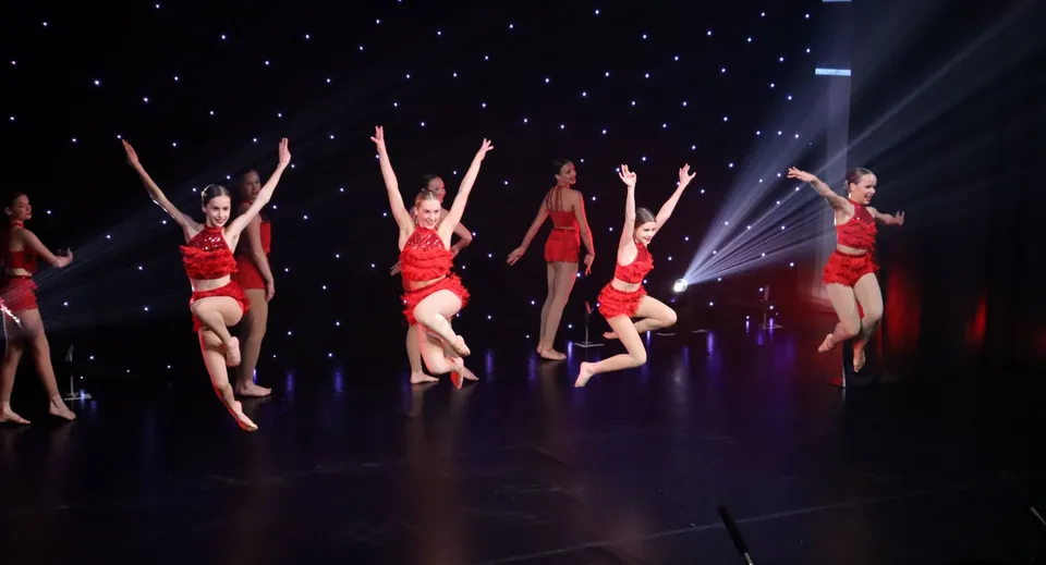 Un gruppo di ballerini in costume rosso esegue una coreografia sul palco della St. Peters School davanti a un cielo stellato.