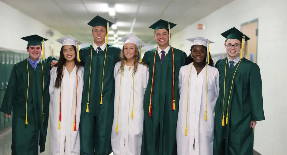 Un gruppo di diplomati in toga verde e bianca si trova nel corridoio del John F. Ross Collegiate Vocational Institute.