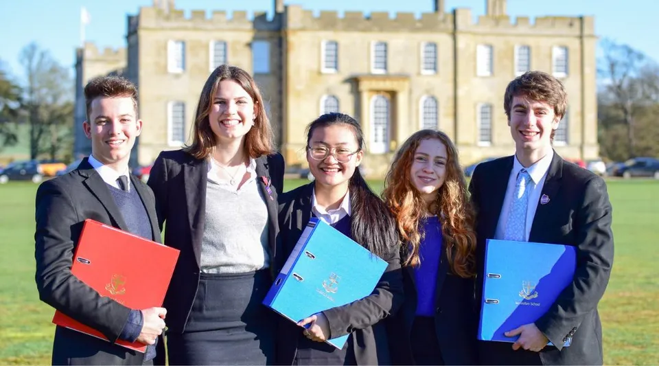 Cinque giovani adulti in abito formale sono in piedi davanti a un edificio storico all'interno del campus della Kimbolton School.