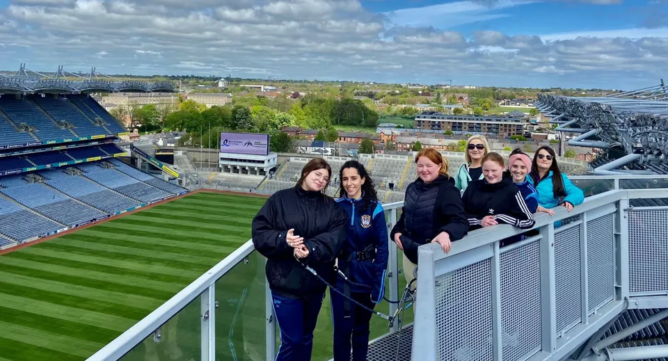 Studenti della Kilkenny City Vocational School si trovano su un balcone con vista su un grande stadio sportivo e la città sullo sfondo.