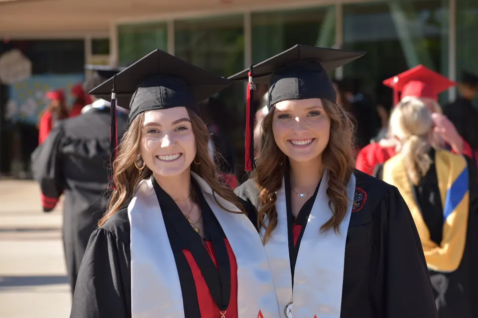 Due studentesse della Murietta Valley High School indossano toghe da laurea davanti a un gruppo di altri diplomati.