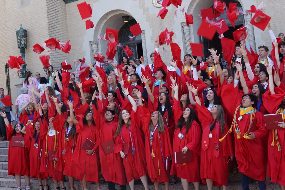 Gli studenti della Incarnate Word Academy si radunano in toghe rosse da diploma sulle scale di un edificio.