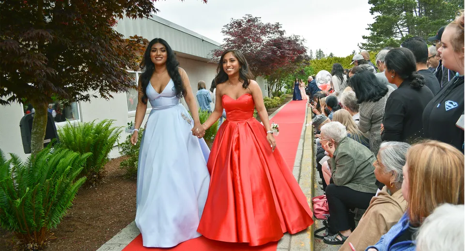 Due studentesse della Delview Secondary School in eleganti abiti da sera camminano sul tappeto rosso in giardino.