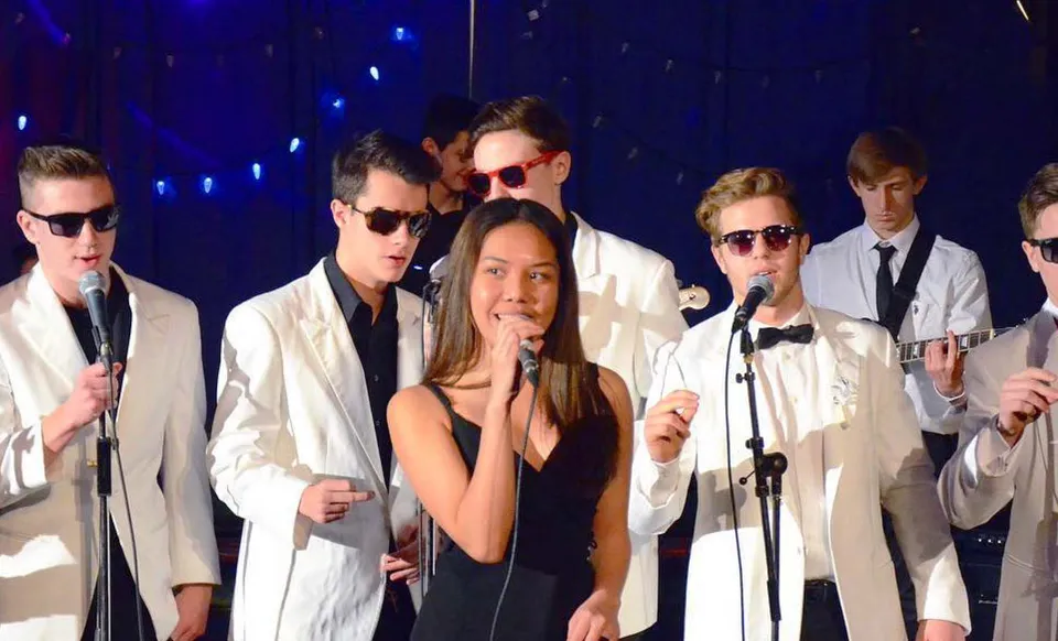 Un gruppo di studenti della Sentinel Secondary School si esibisce su un palco con uno sfondo blu e luci scintillanti.