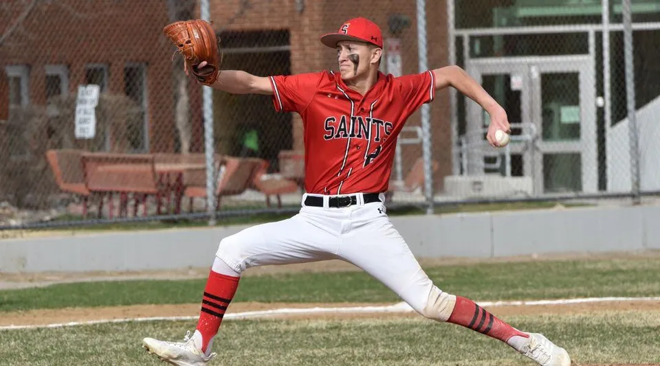 Un giocatore di baseball in divisa rossa dei Saints si trova su un campo da baseball presso le Jeffco Public Schools.