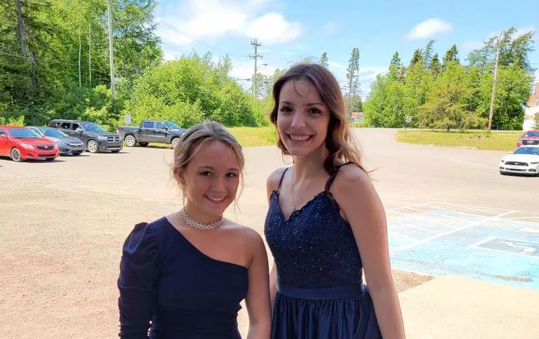 Dos alumnas de la Exploits Valley High School posan juntas con ropa formal en un parque.