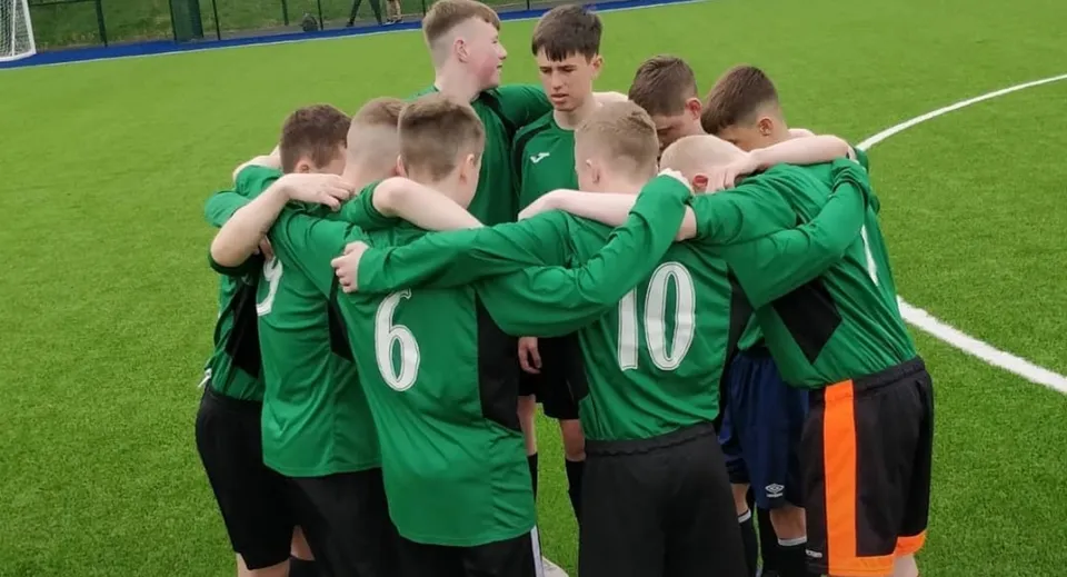 Un gruppo di giovani calciatori in maglia verde sul campo da gioco della Gallen Community School.