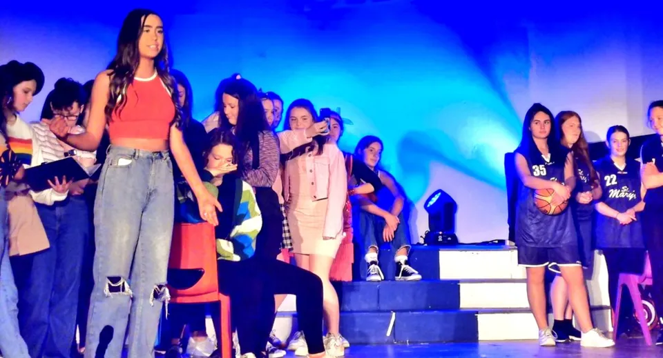 Un gruppo di studentesse della St. Mary’s Secondary School Baldoyle si trova su un palco con luci colorate.