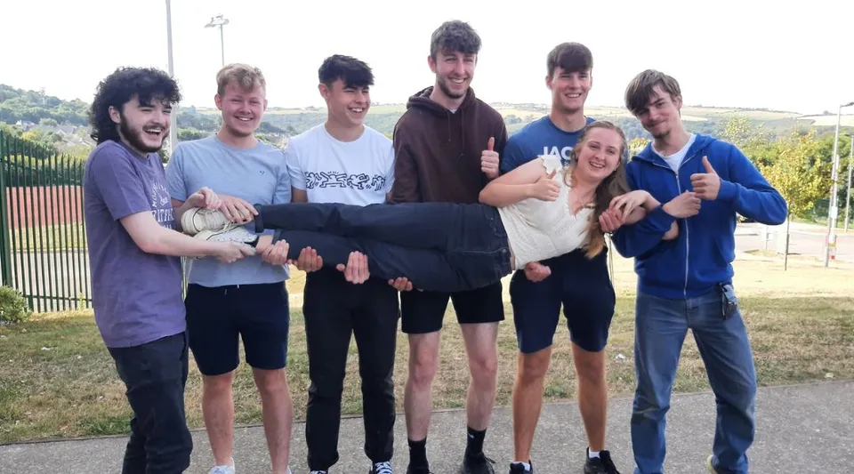Un gruppo di studenti si trova all'aperto su un prato dietro una recinzione nel terreno della Kinsale Community School.