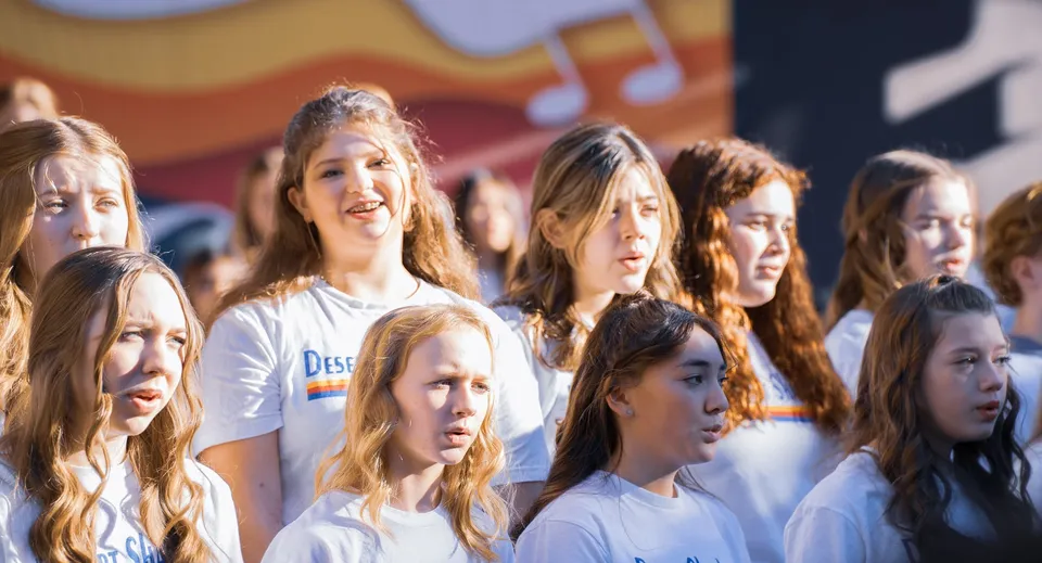 Un gruppo di studentesse del Paradise Valley Unified School District è in piedi insieme in una stanza con spartiti musicali e strumenti sullo sfondo.
