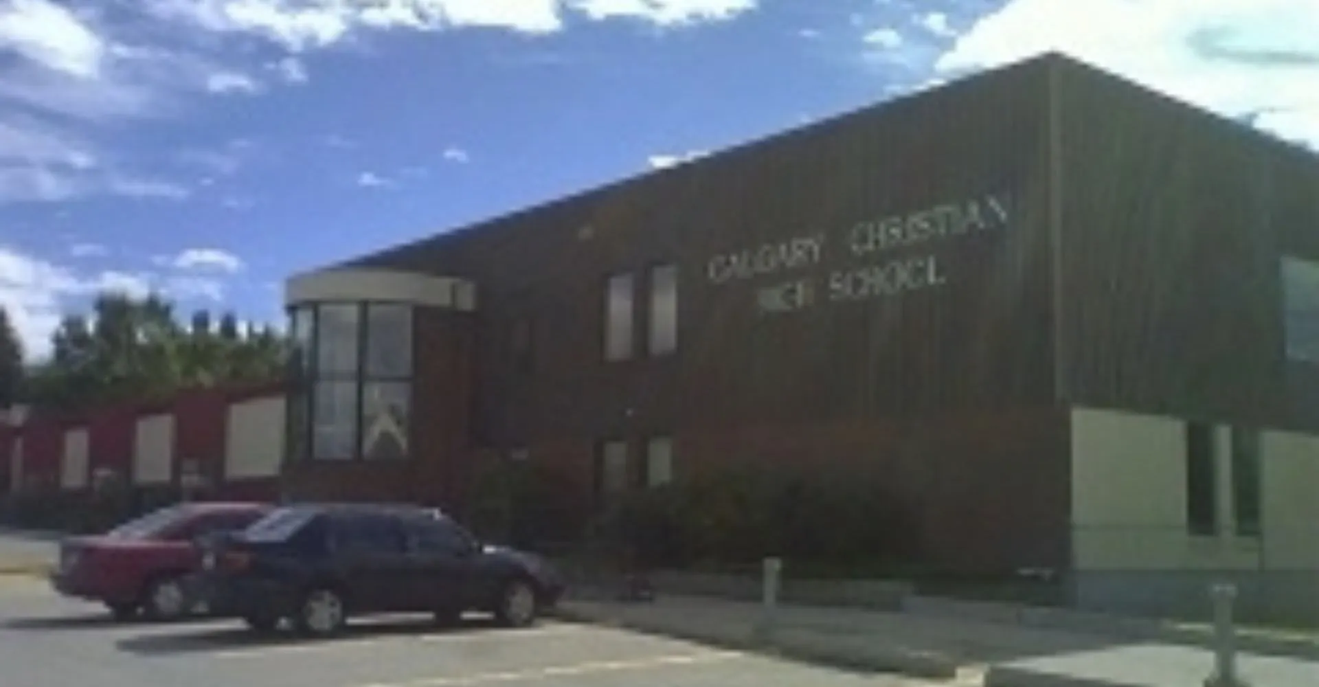 L'ampio edificio della Calgary Christian School con la scritta e un veicolo rosso in primo piano sotto un cielo nuvoloso.